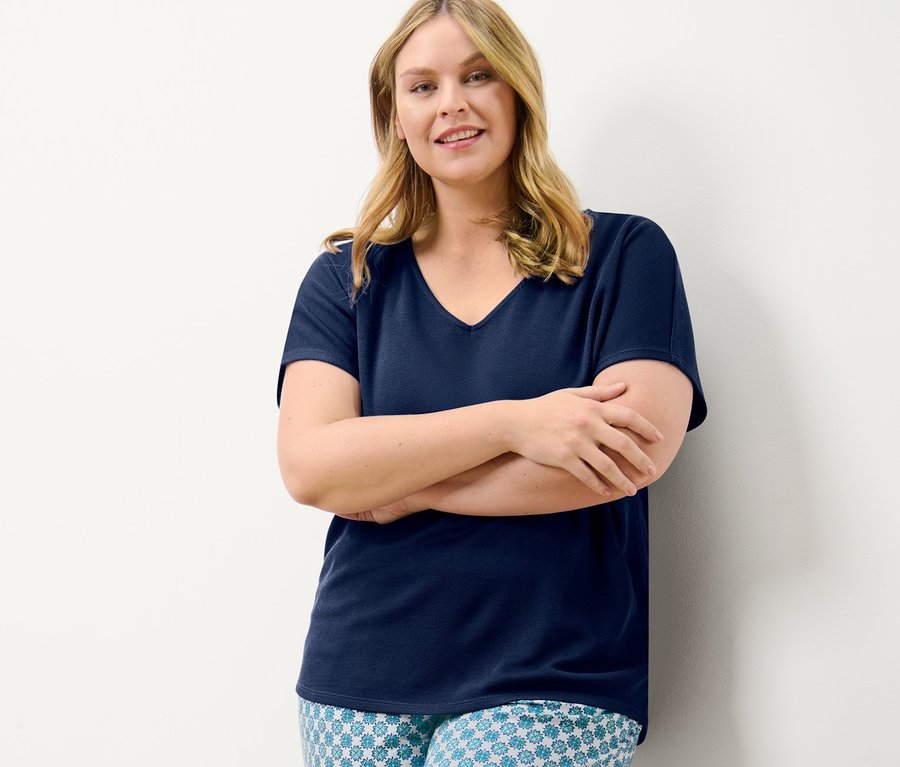 Frau posiert mit verschränkten Armen in einem dunkelblauen, strukturierten Shirt und einer Jerseyhose mit Alloverprint.