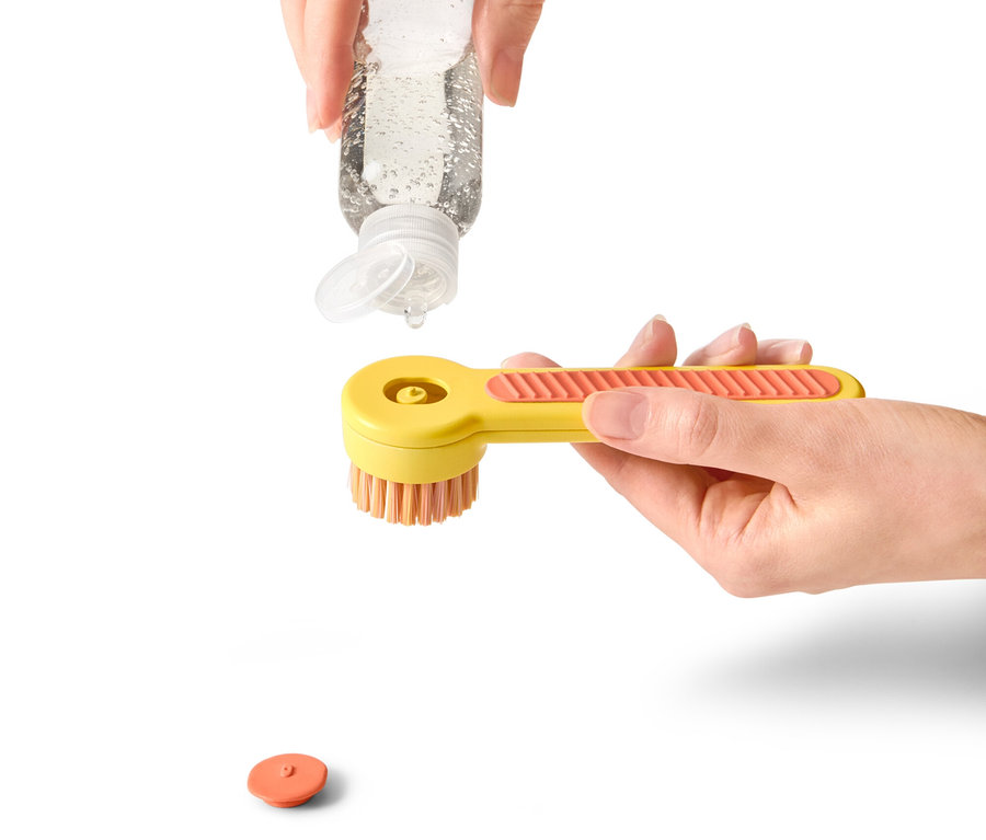 Hand gießt Reinigungslösung auf gelbe Schuhbürste.