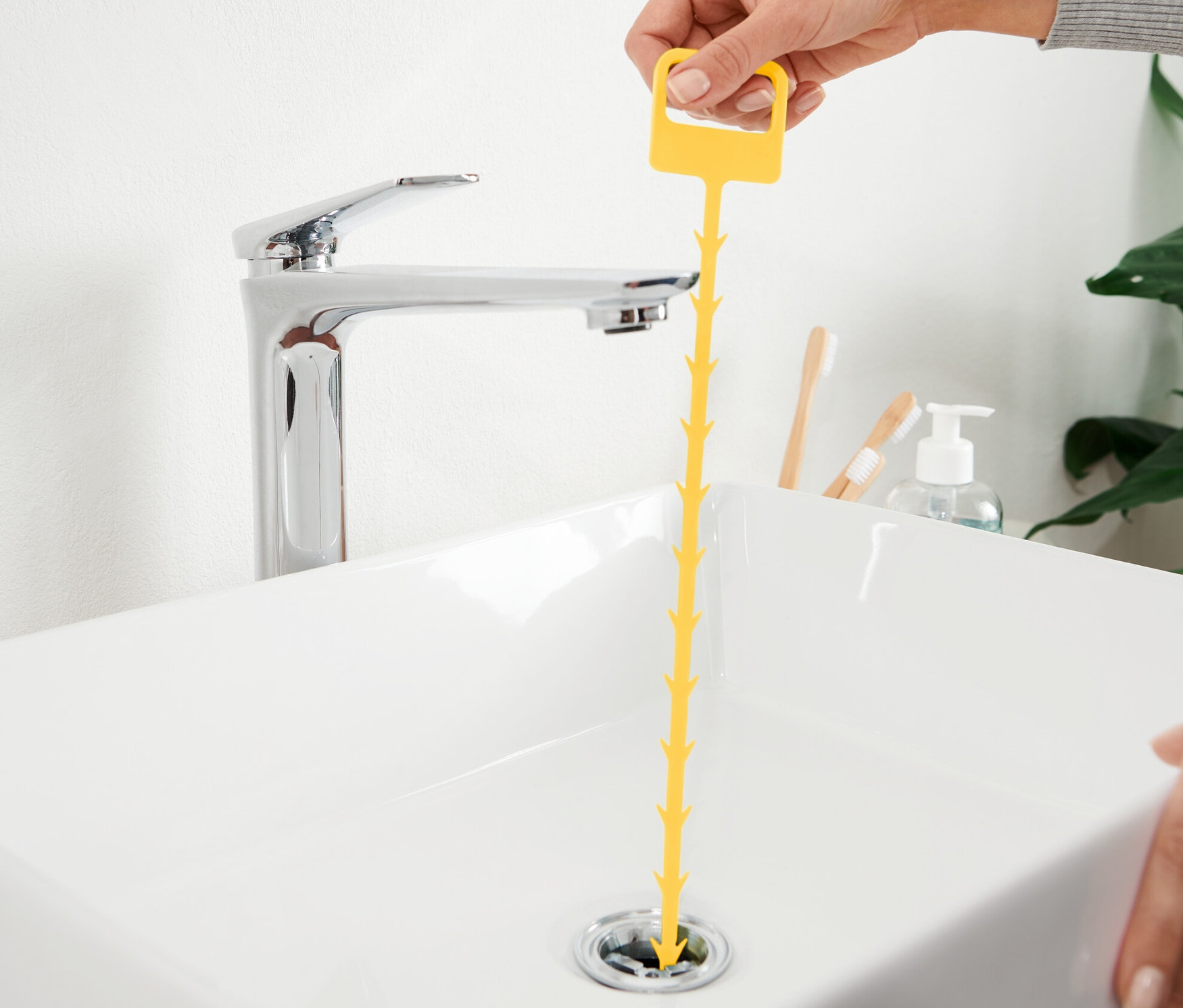 Eine Hand führt einen gelben 2 Abflussreiniger in ein weisses Waschbecken ein.