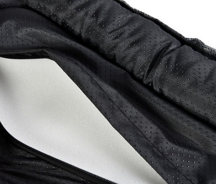 Eine Hand öffnet ein schwarzes Outdoor-Hundebett mit Reißverschluss, wobei die weiße Schaumstofffüllung im Inneren sichtbar ist.