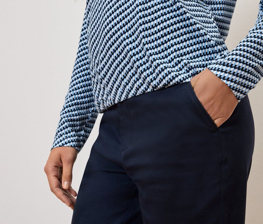 Teilansicht einer Person mit der Hand in der Hosentasche und einem blau-weißen Oberteil.