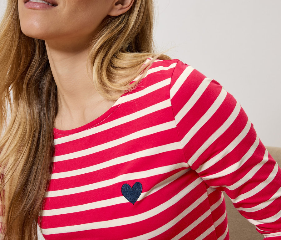 Blonde Frau trägt rot-weiß gestreiftes Langarmshirt mit dunkelblauem Herz.