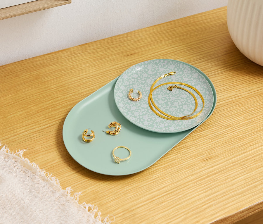 Goldschmuck liegt auf dekorativen Tellern auf einem Holztisch.