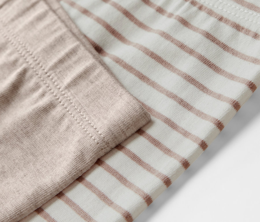 Detailaufnahme von 5 Kinder-Leggings, eine beige, die andere mit braunen Streifen.