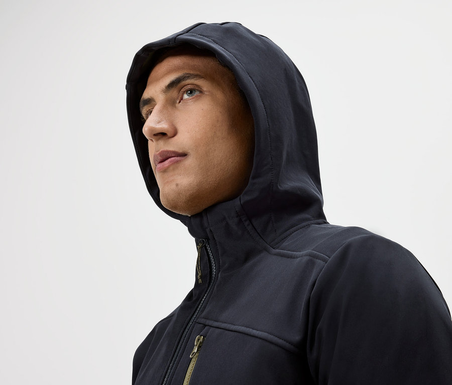 Porträt eines Mannes mit Kapuze und Reißverschlussjacke, der auf einem weißen Hintergrund nach oben schaut.