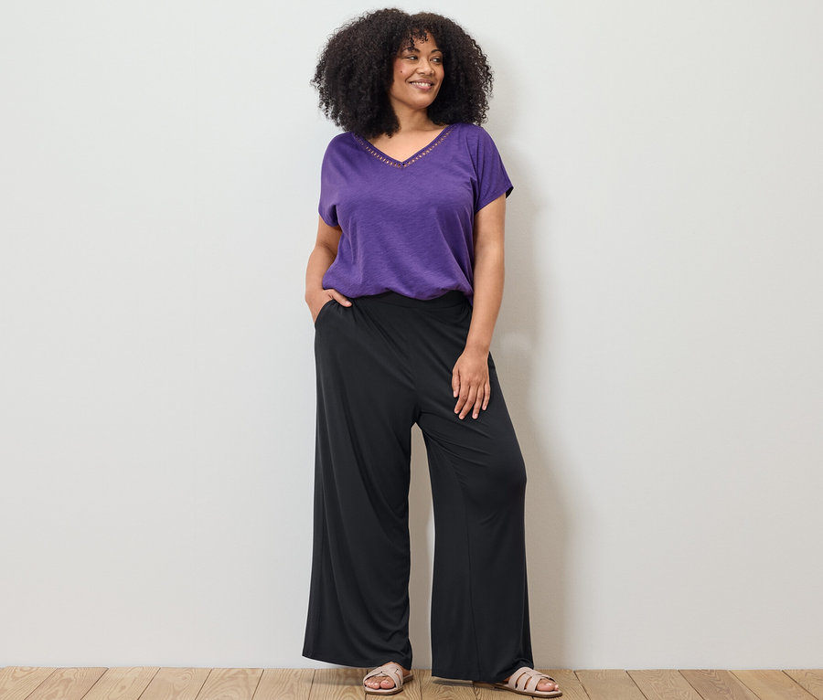 Frau posiert in lila Shirt aus Modalmix und schwarzer Palazzohose.