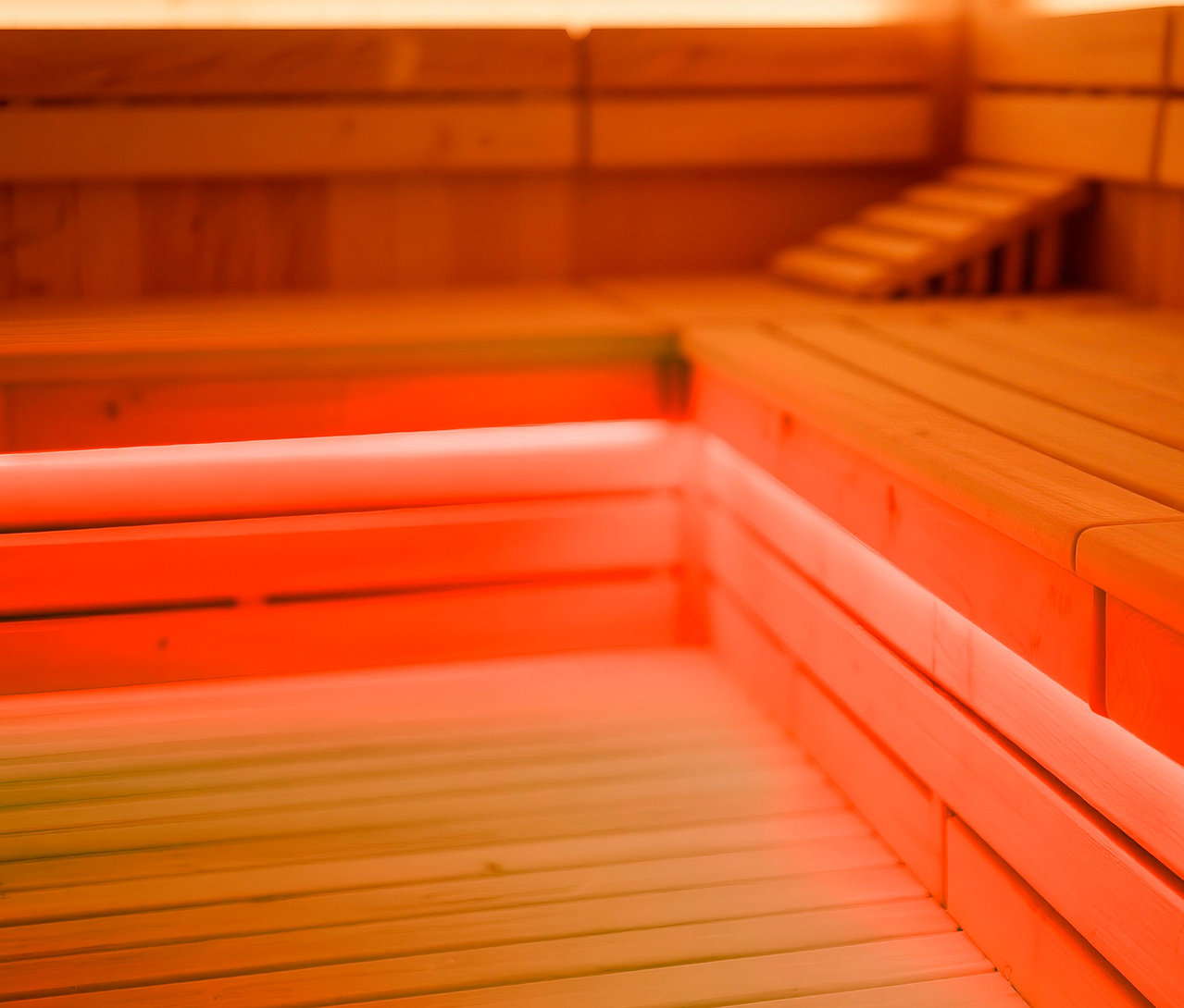 Innenansicht einer Sauna mit Holzverkleidung und Bänken, beleuchtet mit rotem Licht.