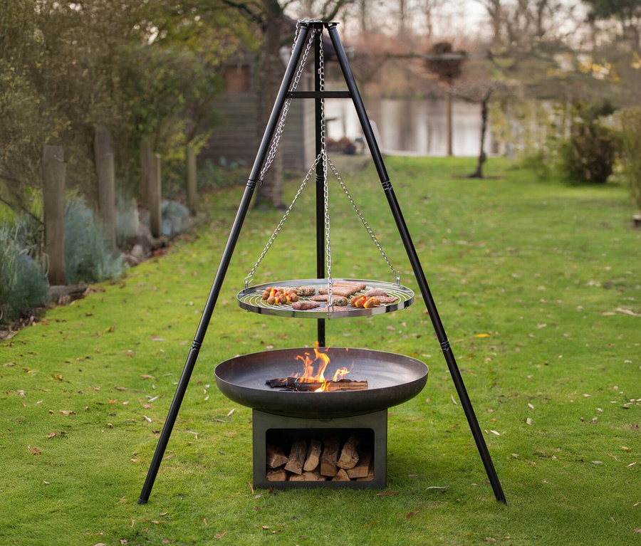 Eine »Juva Industrial« Feuerschale, ca. 80 cm, steht im Garten, über dem Feuer hängt ein Grillrost mit Grillgut.