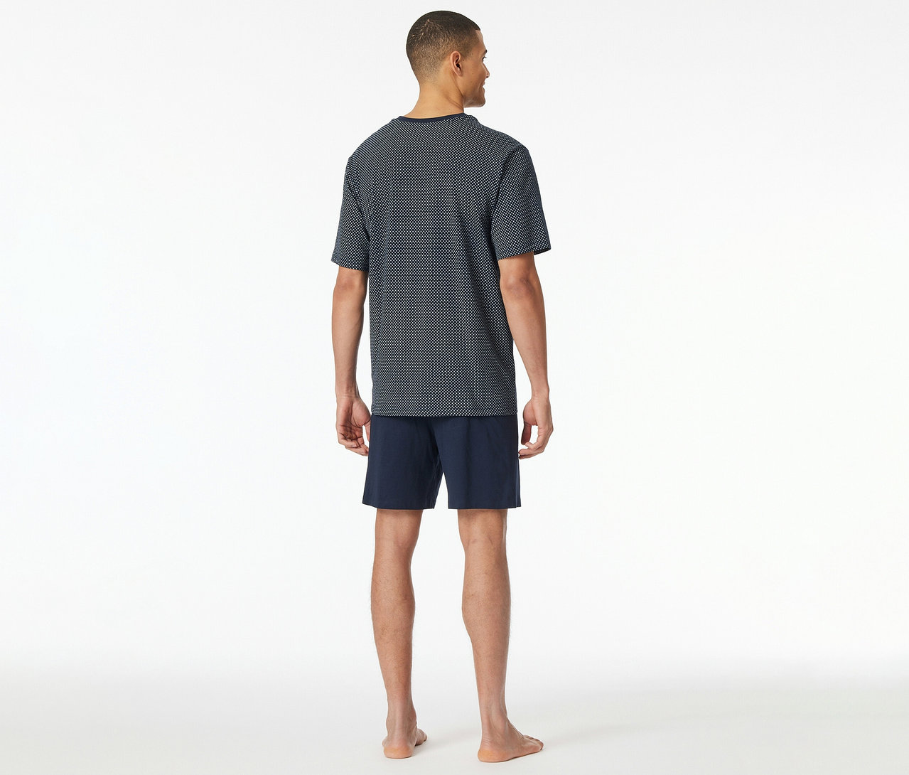 Mann von hinten im SCHIESSER Shorty-Pyjama-Set mit blau gemusterter T-Shirt-Oberseite und marineblauen Shorts.