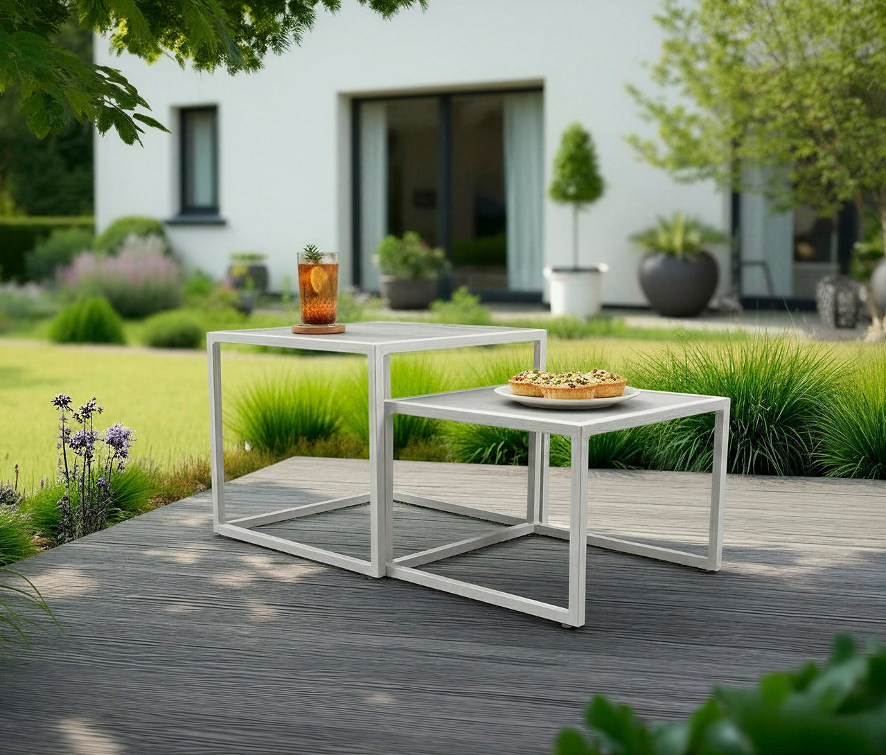 Auf zwei weißen, quadratischen Tischen im Freien stehen ein Getränk und ein Teller mit Törtchen.