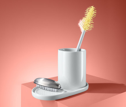 Ein Spülutensilien-Ständer mit einer gelben Bürste steht auf einem rosa Podest.