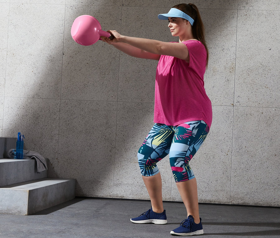 Frau trainiert mit pinkem Sportshirt und 3/4-Sporttights mit einer rosa Kettlebell.