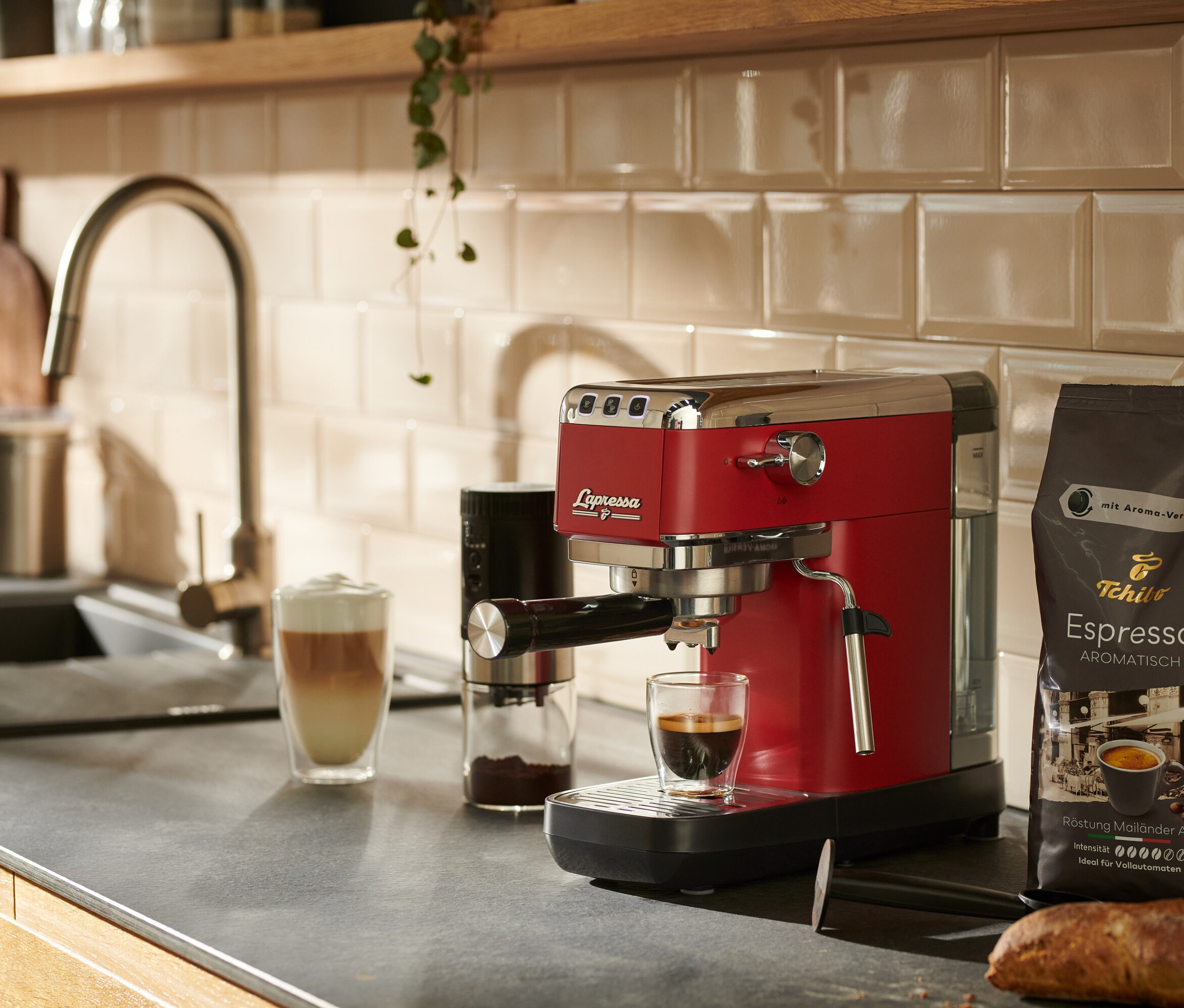 Eine rote »Lapressa« Siebträgermaschine steht auf einer Küchentheke neben einem Glas Kaffee.