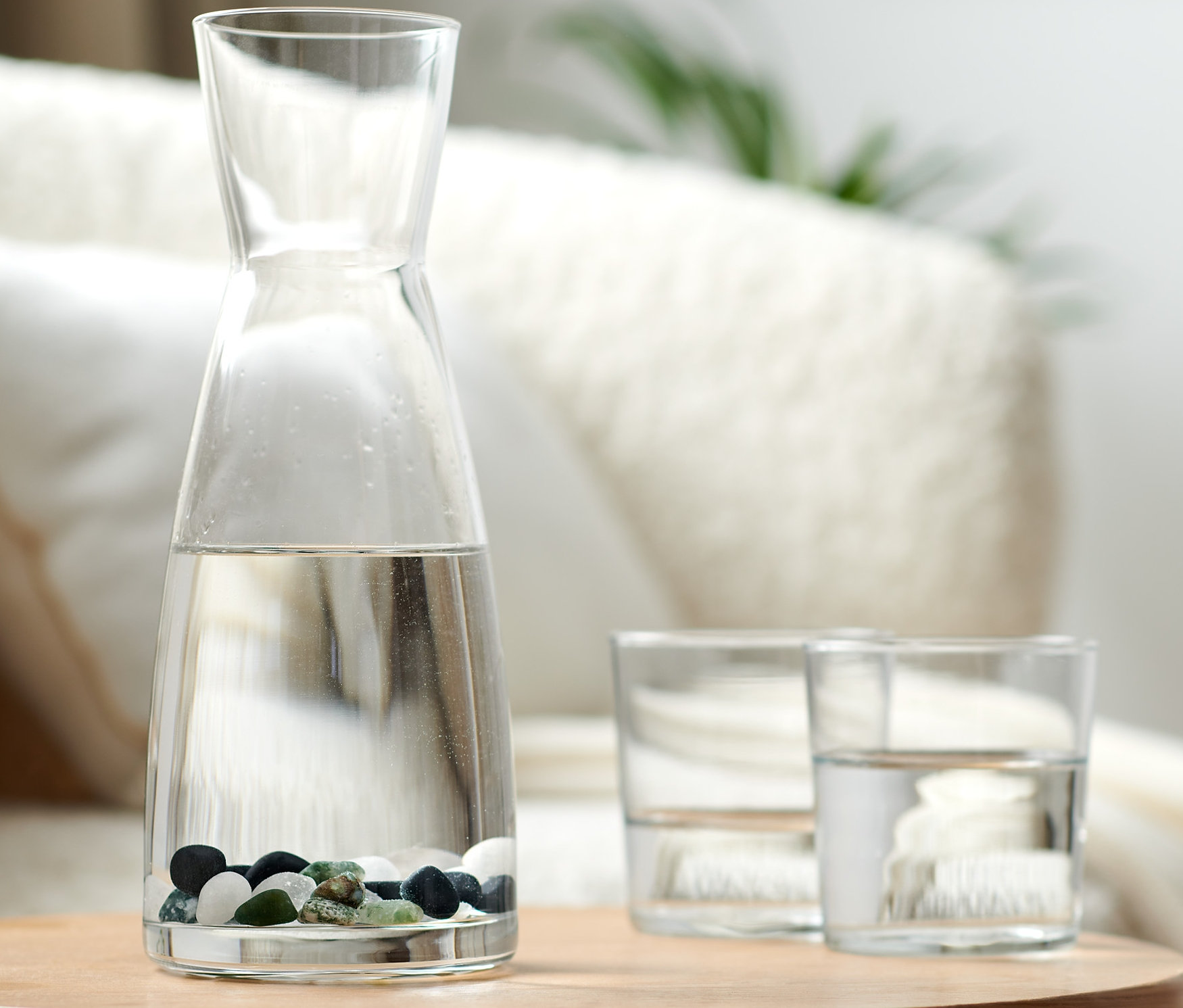 Glaskaraffe mit Wasser und Wassersteinen auf einem Holztisch.