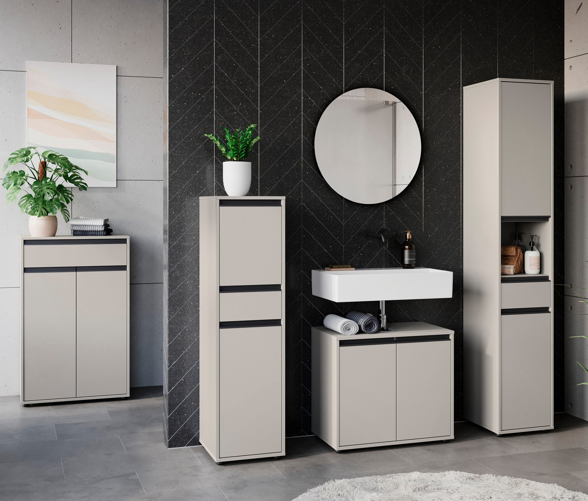 Ein Badezimmer mit Waschbecken, Spiegel und Schränken. Im Vordergrund steht ein »Lemont« Hochschrank in Steingrau.