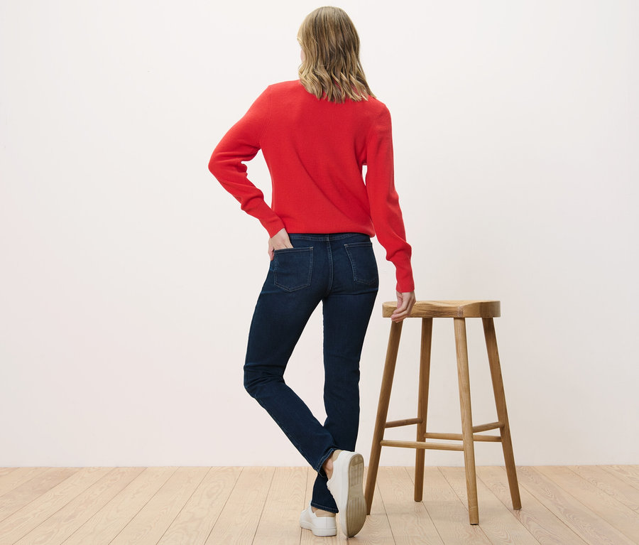 Frau steht mit dem Rücken zur Kamera und trägt eine Slim Jeans – Fit »Emma« und einen roten Pullover.