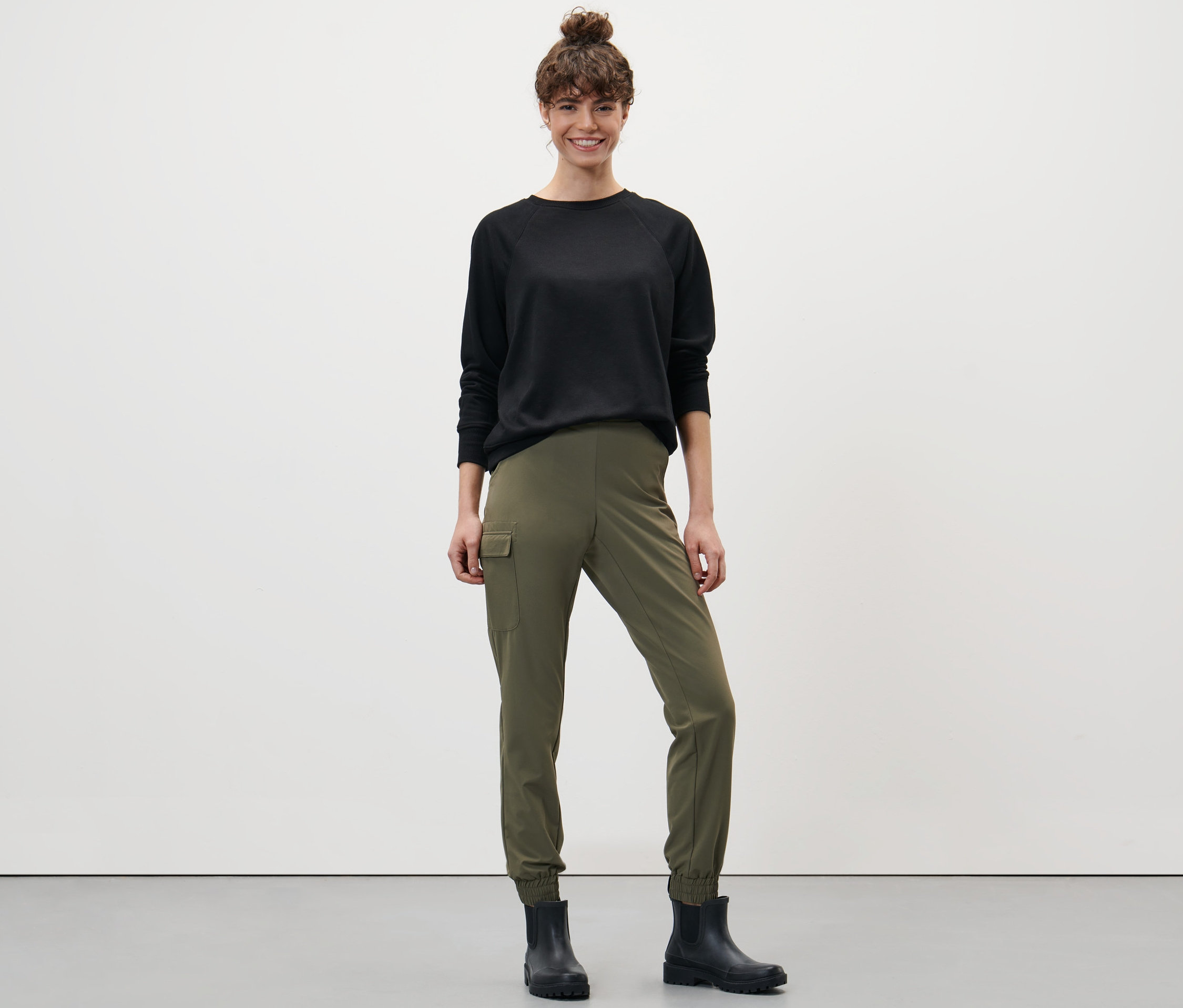 Frau steht und trägt ein schwarzes Oberteil und eine khaki Softshel-Joggpants.