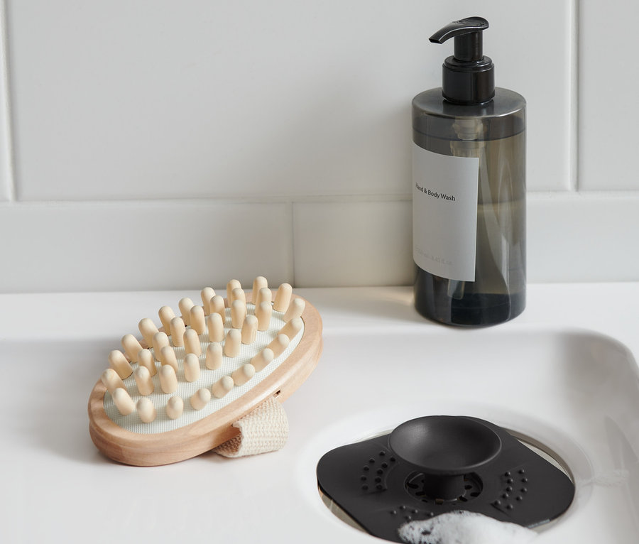 Im Waschbecken befindet sich ein Abflusssieb/-verschluss, daneben liegen eine Massagebürste und eine Seifenflasche.