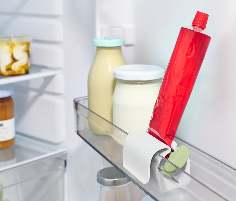 Eine rote Tube steckt in einem Tubenpresser mit Kühlschrankclip im Kühlschrankregal neben anderen Lebensmitteln.