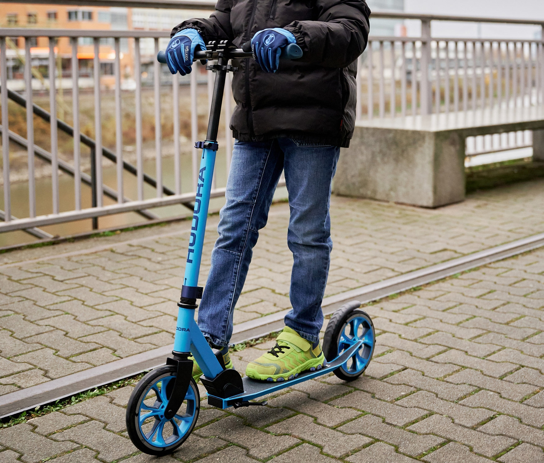Ein Junge auf einem blauen HUDORA Scooter Up 200 auf dem Gehweg.