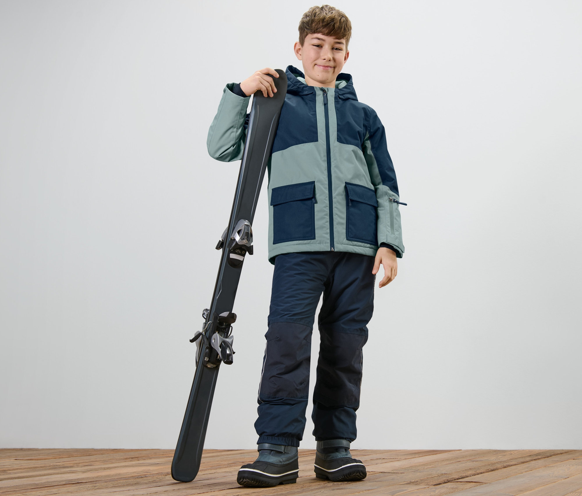 Junge mit Kinder-Outdoor-und-Snowboardjacke hält Ski.