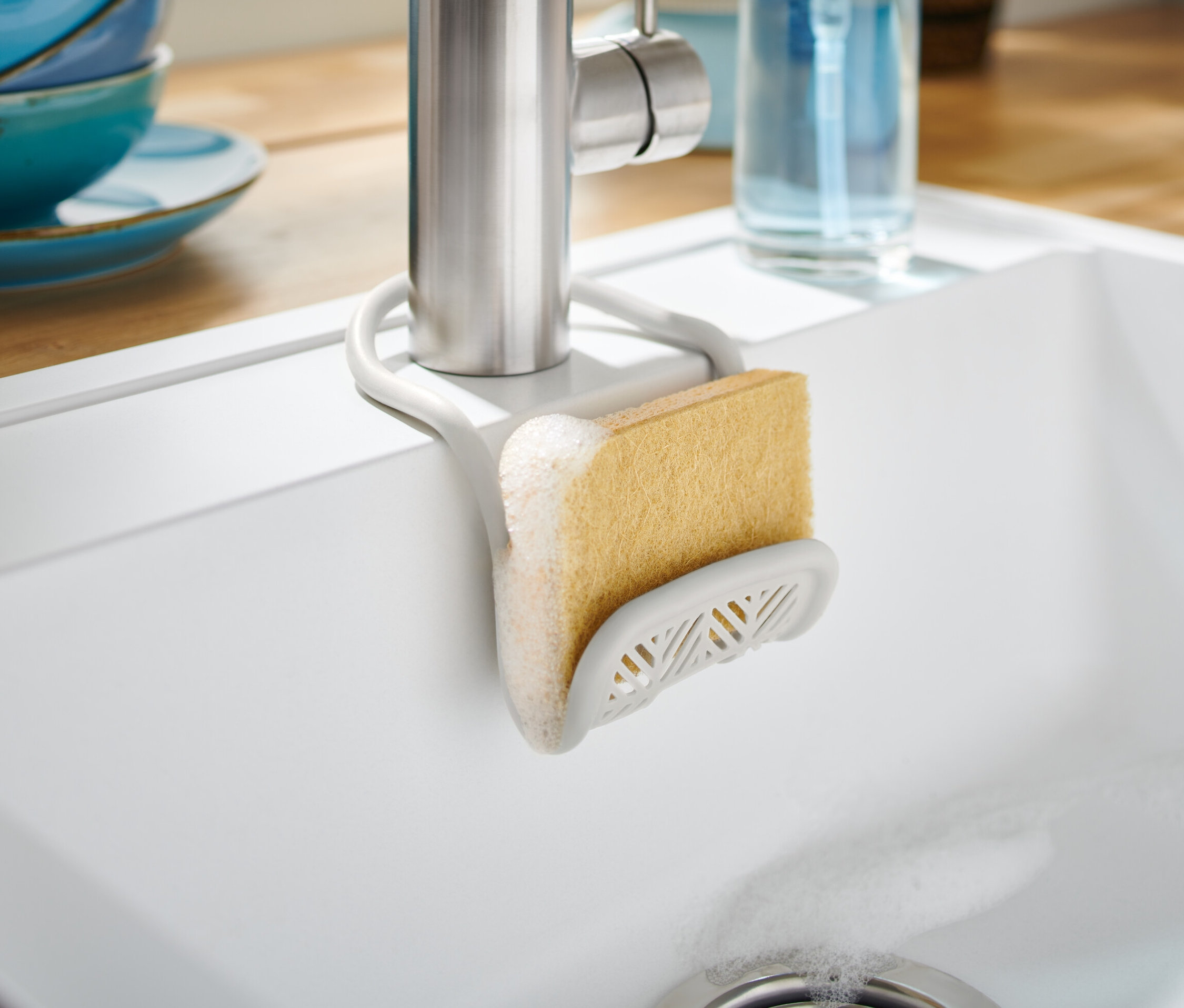 Schwammhalter mit Schwamm an einem Wasserhahn in einem weißen Waschbecken befestigt.