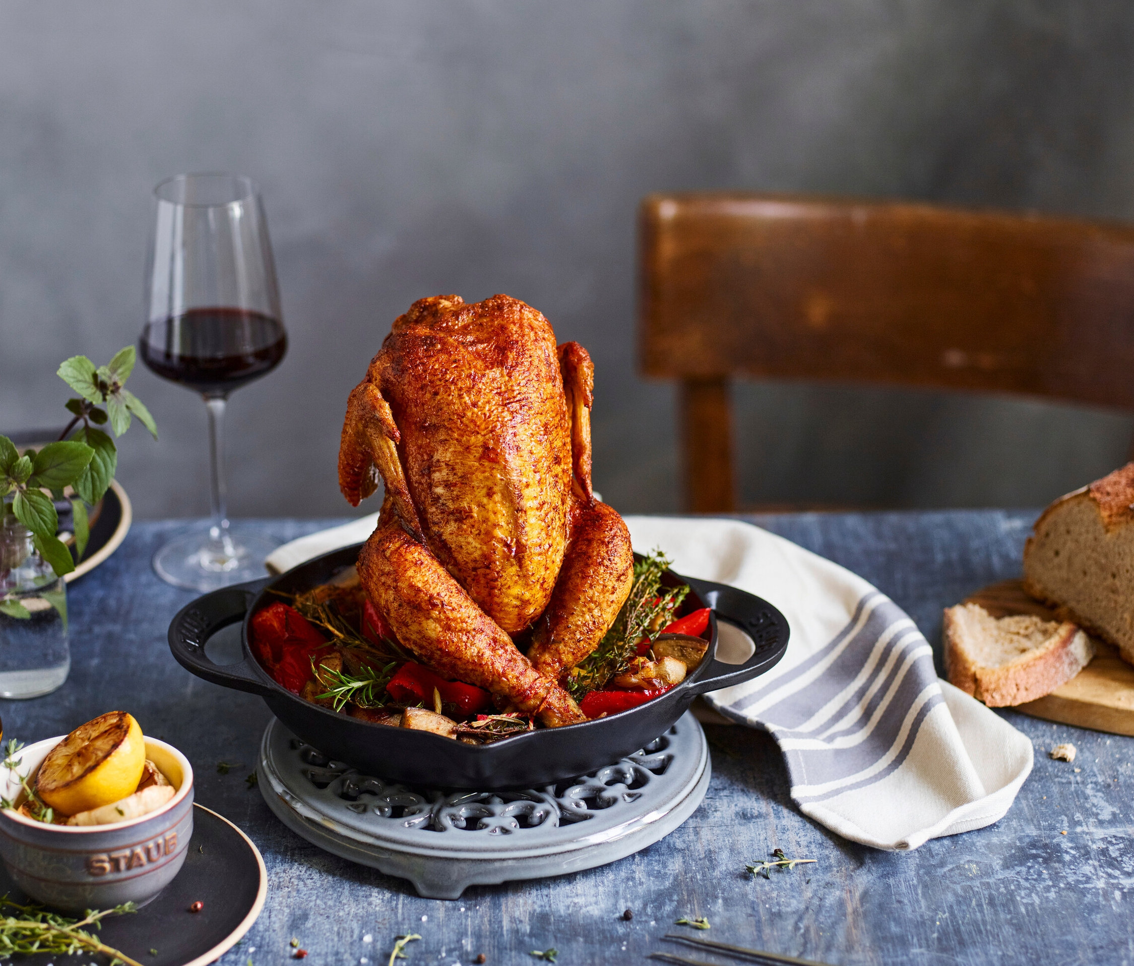 Ein aufrecht gebratenes Hähnchen in einem schwarzen STAUB Hähnchen-Bräter mit gebratenem Gemüse.