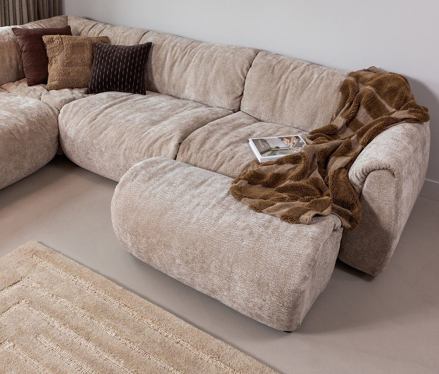Beiges Ecksofa mit braunen Kissen und Überwurf. Auf dem Boden liegt ein beiger Teppich »Alicia« von Woood.
