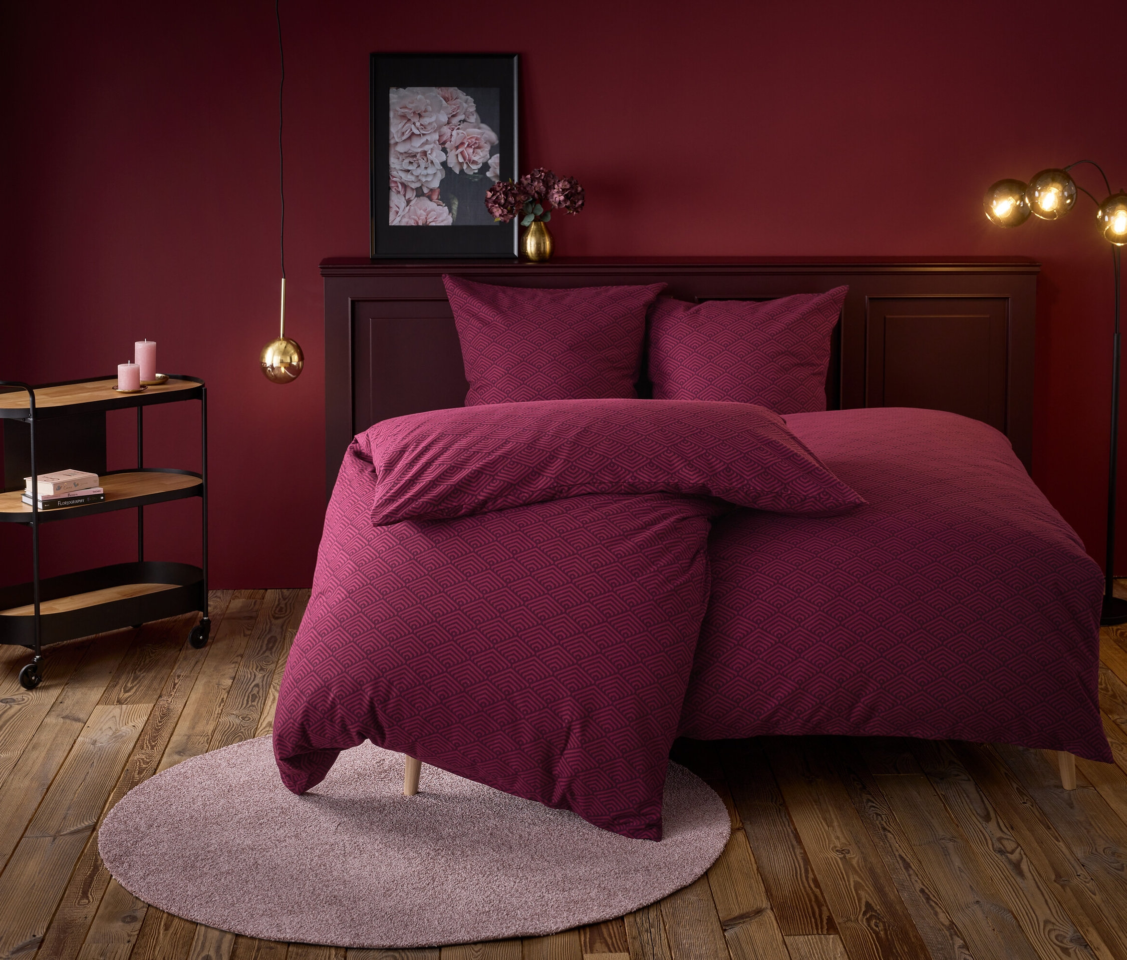 Weinrotes Schlafzimmer mit einem Bett mit geometrischem Muster, einem runden Teppich und einem Servierwagen.