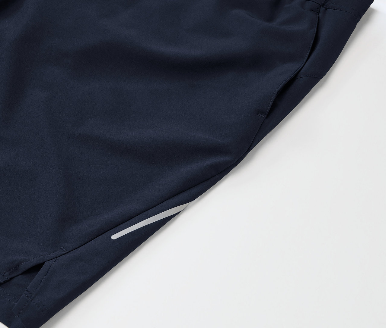 Detailaufnahme von marineblauen Sportshorts mit Tasche und reflektierendem Detail am Bein.