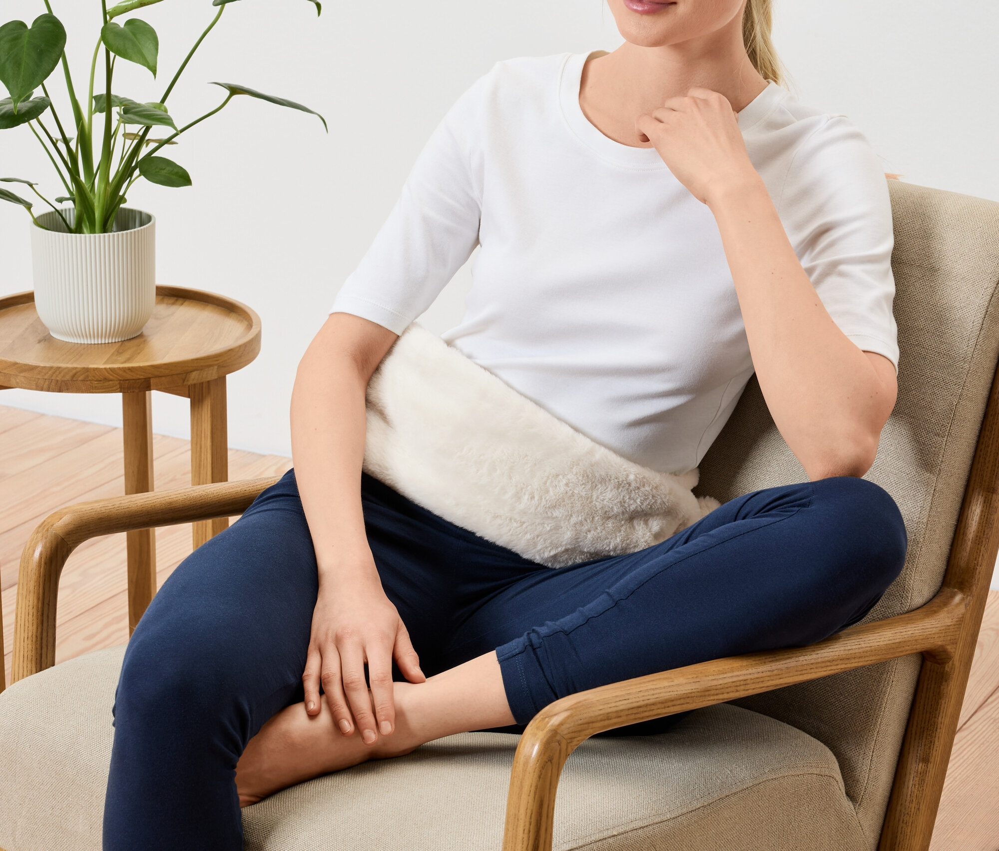 Frau sitzt mit Wärmekissen auf dem Bauch im Sessel.