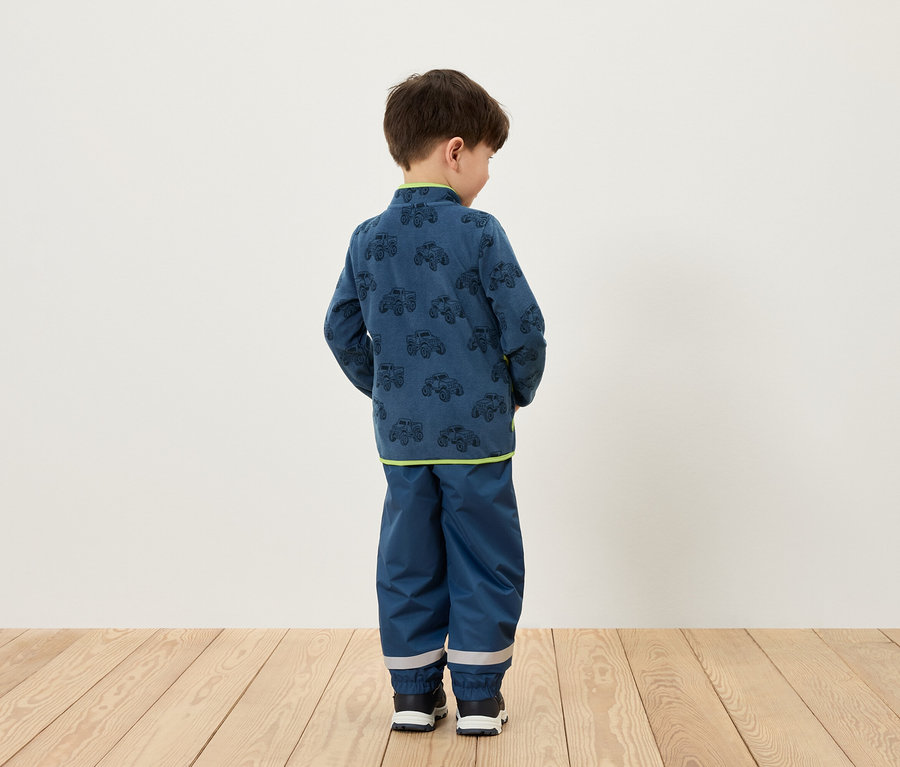 Junge steht mit dem Rücken zur Kamera und trägt blaue Kleidung mit einem Autoaufdruck.