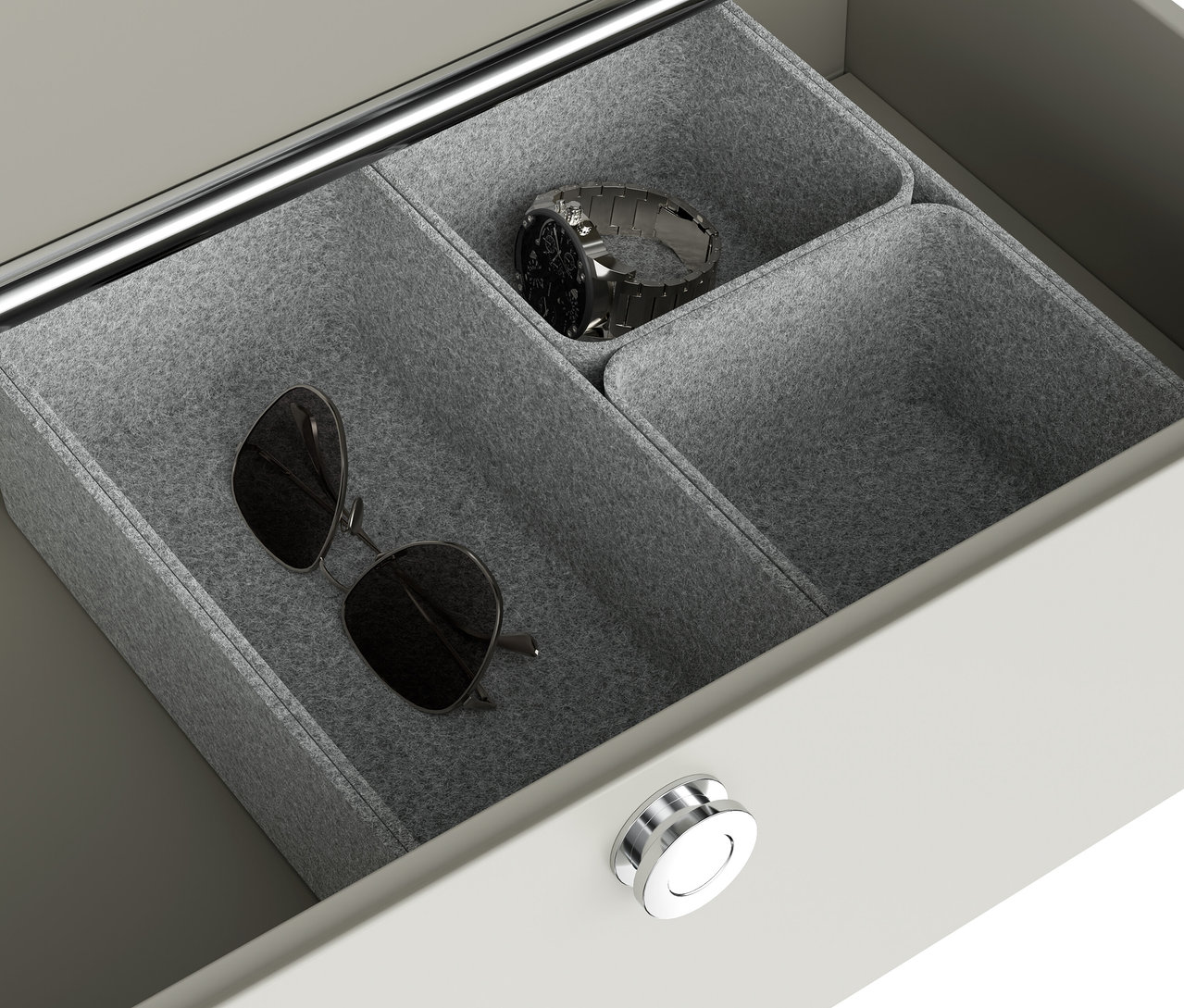In einer offenen Schublade liegen in grauen Filzschalen eine Sonnenbrille und eine silberne Uhr.
