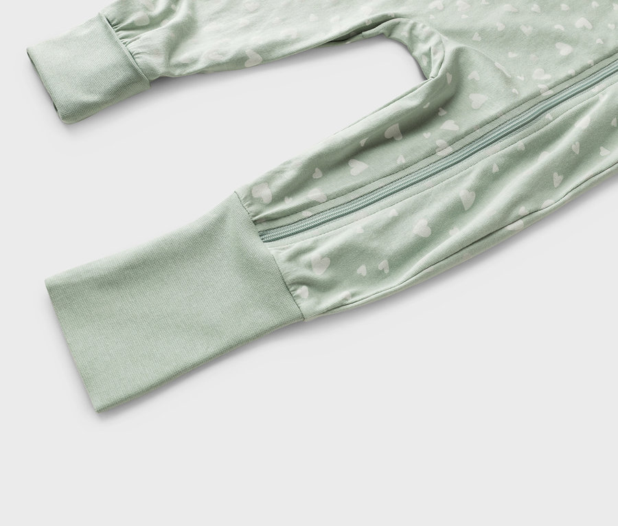 Nahaufnahme eines hellgrünen Baby-Schlafanzugs mit weißem Herzmuster und Reißverschluss.