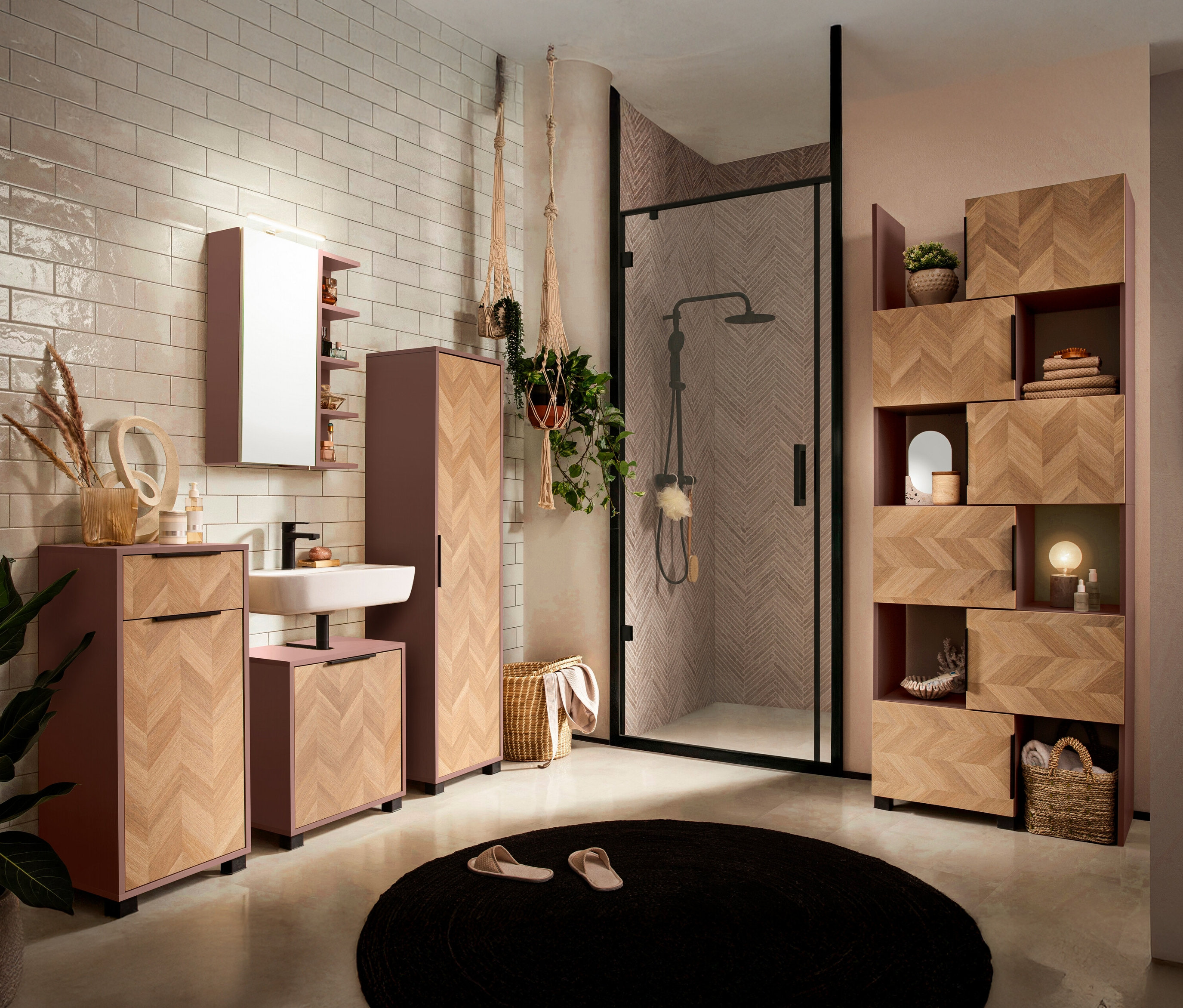 Badezimmer mit Waschbecken, Spiegelschrank, Hochschrank und Regal in Holzoptik und rosa Akzenten. Runde, schwarze Matte und Dusche mit schwarzem Rahmen.