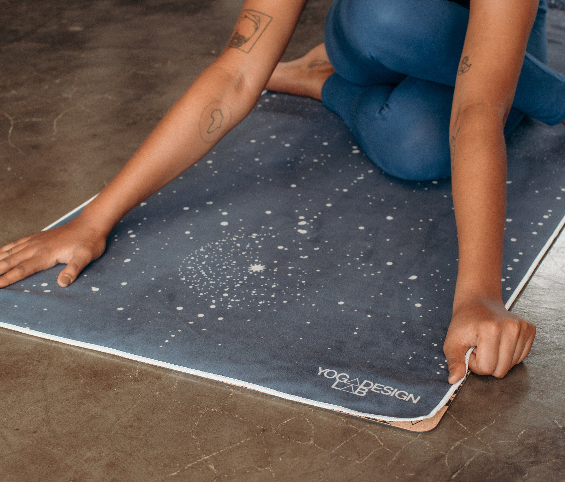 Frau sitzt auf einer Yogamatte mit Sternenmuster und berührt deren Rand.