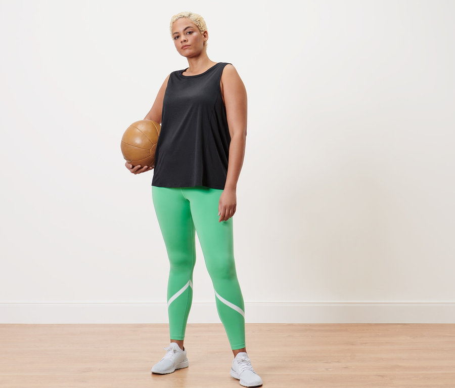 Frau hält einen Volleyball, trägt grüne Sporttight und ein anthrazitfarbenes Sport-Top.