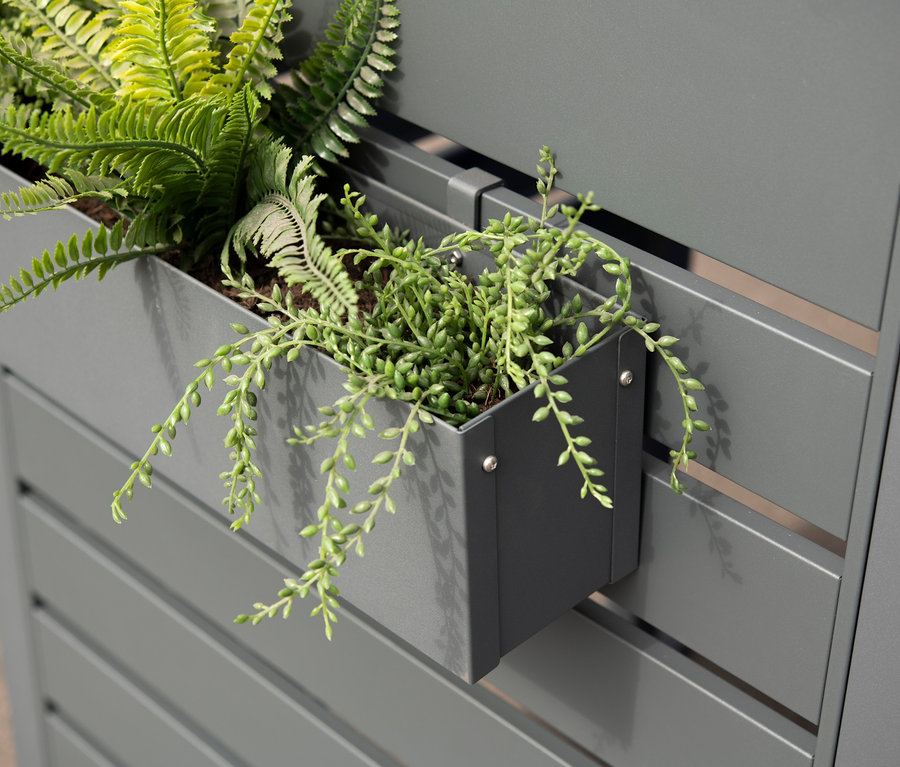 Grauer Blumenkasten aus Stahl mit Pflanzen an einer grauen Zaunwand befestigt.