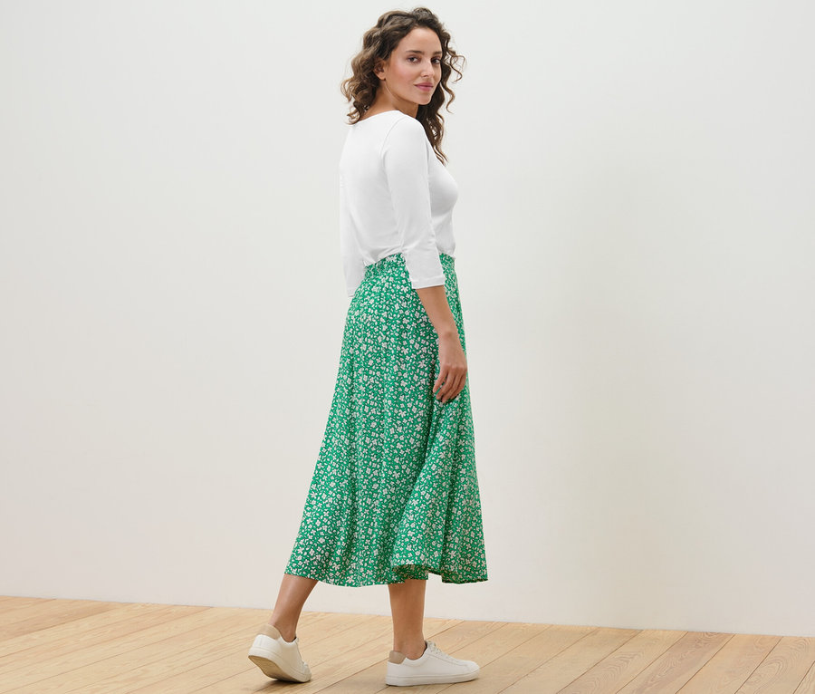 Frau posiert in einem grünen bedruckten Midirock und einem weißen Oberteil.
