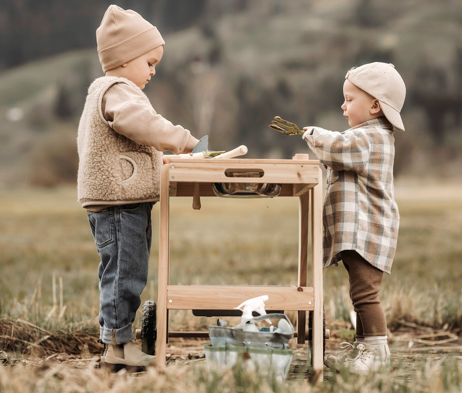 Zwei Kinder spielen draußen mit einer kompakten small foot Matschküche und einem großen small foot Gartenwerkzeug-Set.