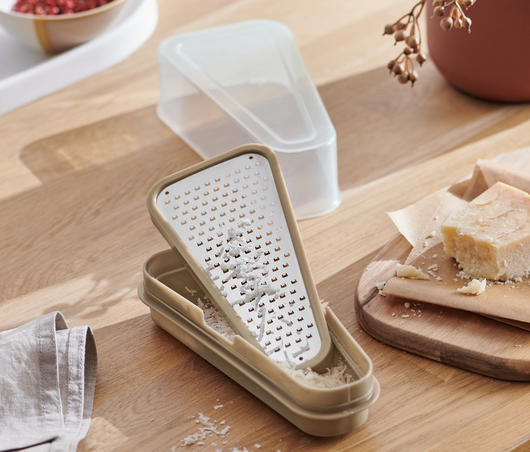 Draufsicht auf eine 2-in-1-Parmesanreibe mit Behälter auf einem Holztisch, zusammen mit Lebensmitteln.