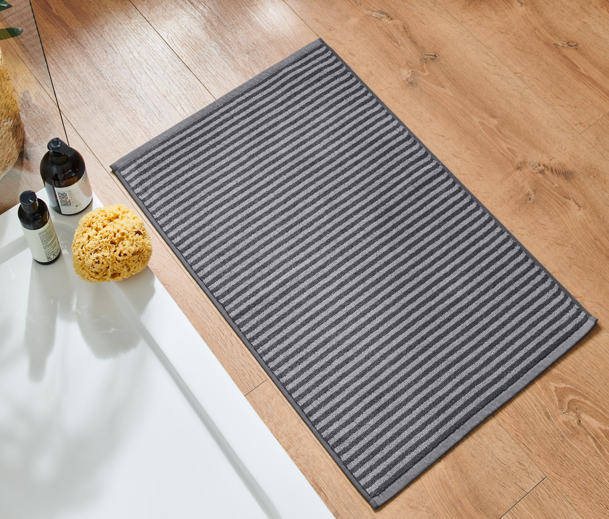 Ein hochwertiger, anthrazitfarbener Duschvorleger liegt auf einem Holzboden neben einer Dusche.