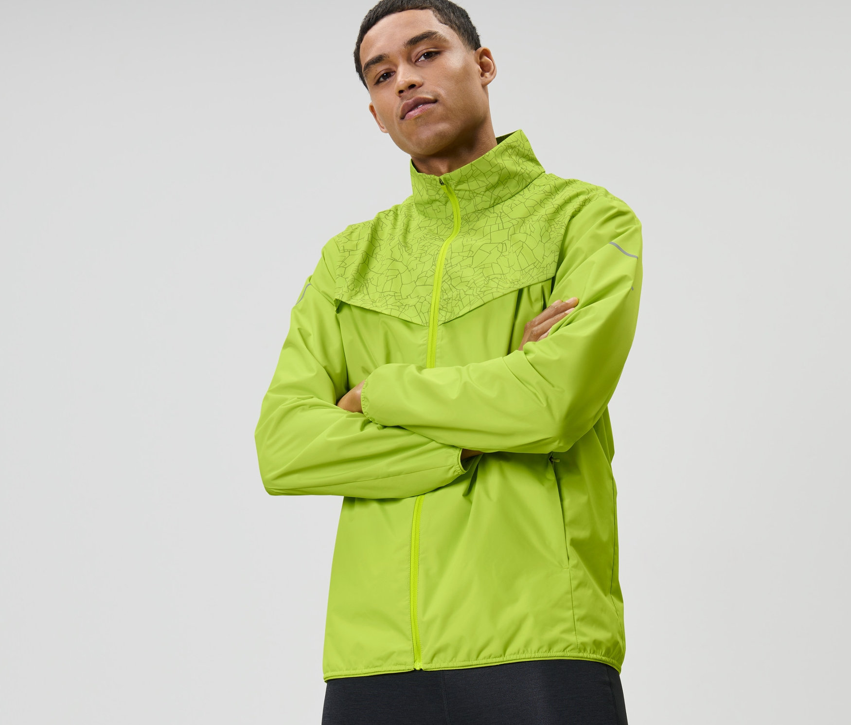 Mann mit verschränkten Armen trägt neonlime Windprotection-Laufjacke.