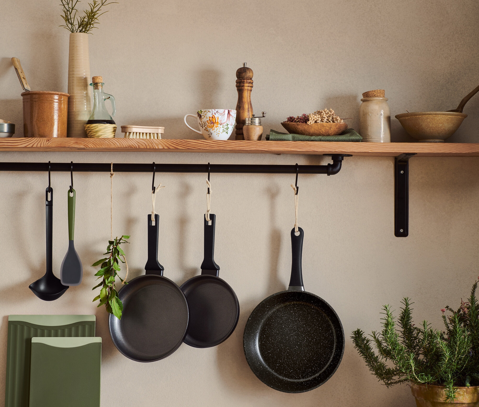 In einer Küche hängen Pfannen und Schöpfkellen an der Wand. Auf der Küchentheke liegen zwei Schneidebretter, Pilze und Kräuter.