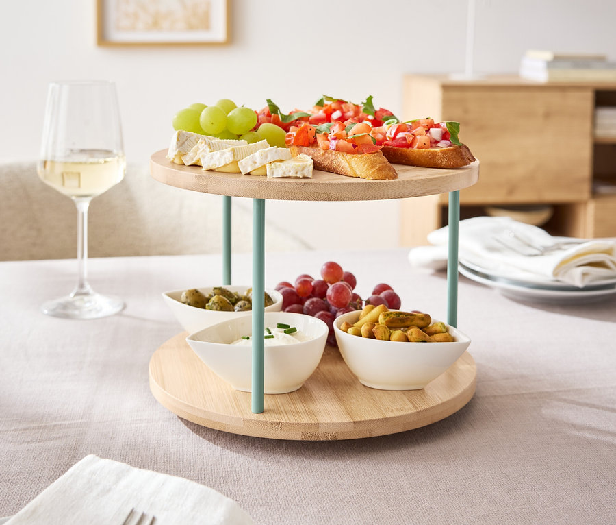 Eine drehbare Etagere mit Snacks wie Bruschetta, Käse und Obst steht auf einem Tisch.
