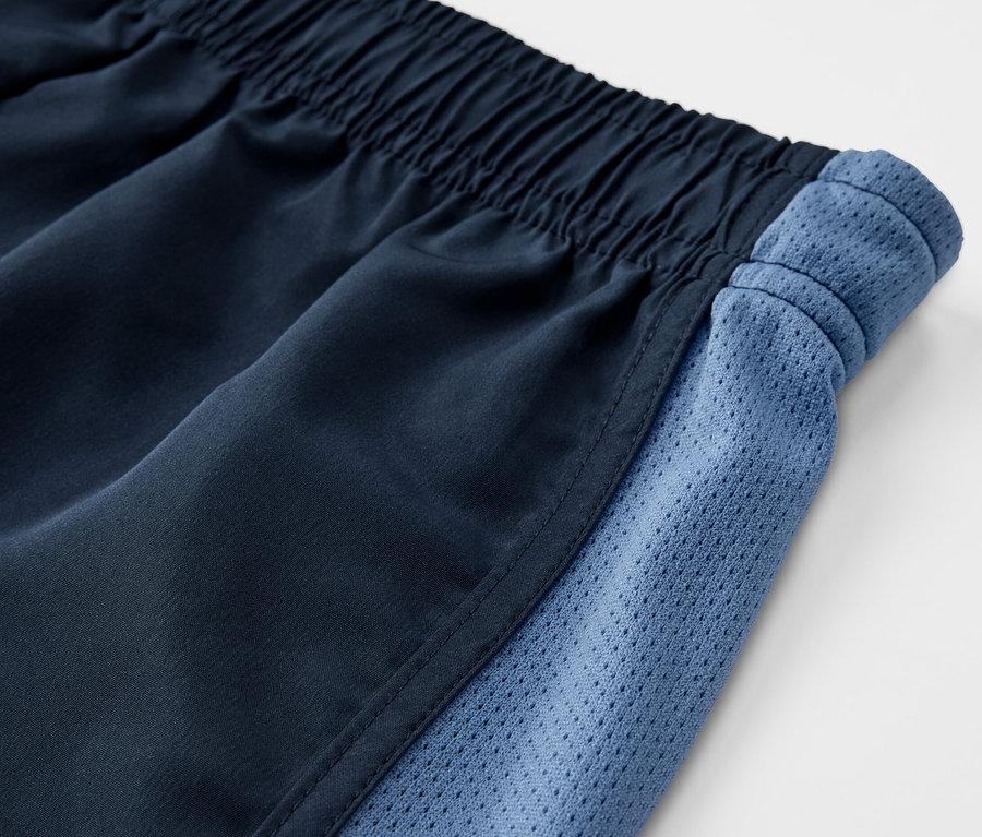 Detailansicht einer 2er-Packung Kinder-Sportshorts mit elastischem Bund und blauen Mesh-Einsätzen an der Seite.