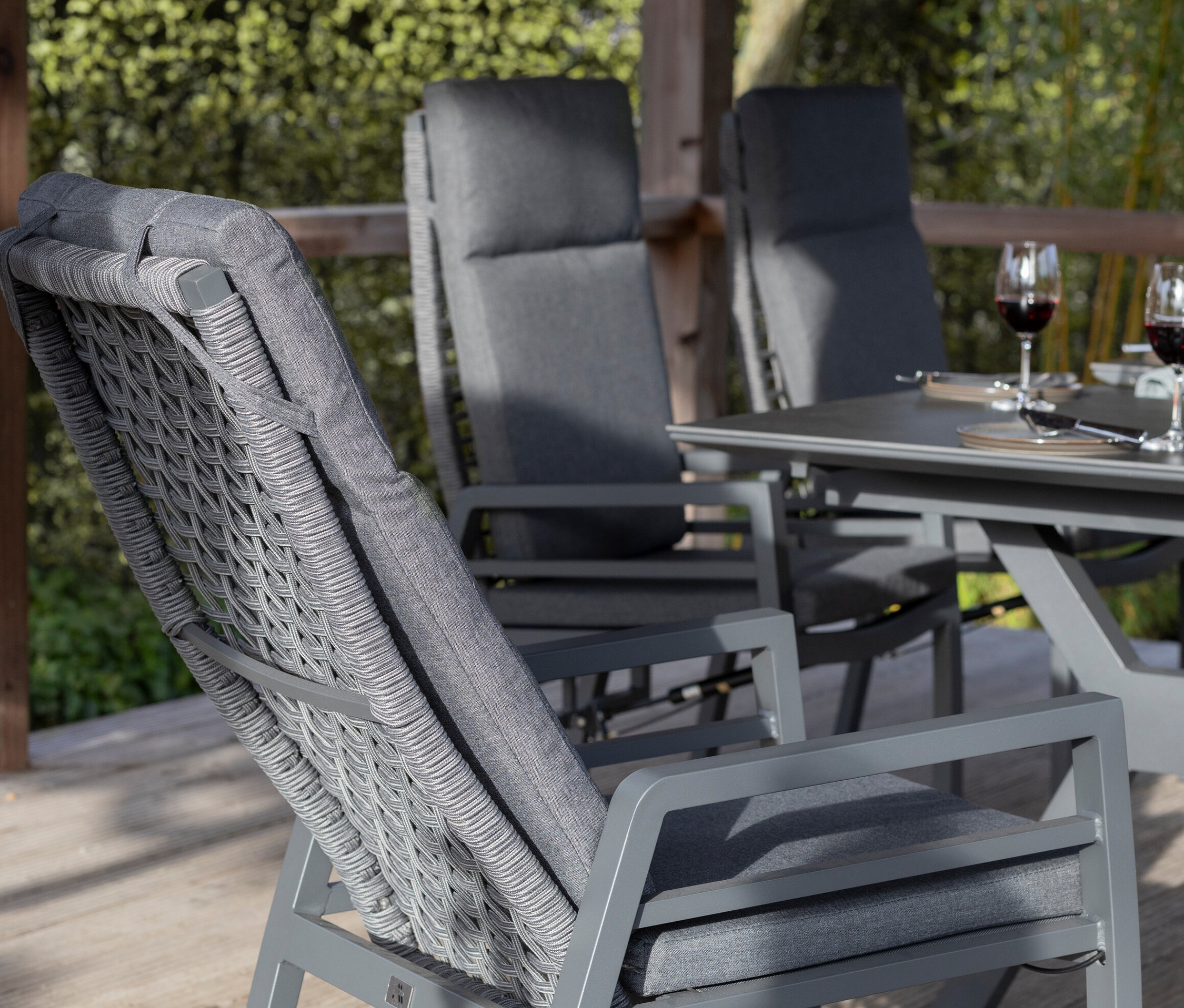 Graues deVries Dining-Set mit Seiloptik auf einer Terrasse; auf dem Tisch stehen Weingläser und Snacks.