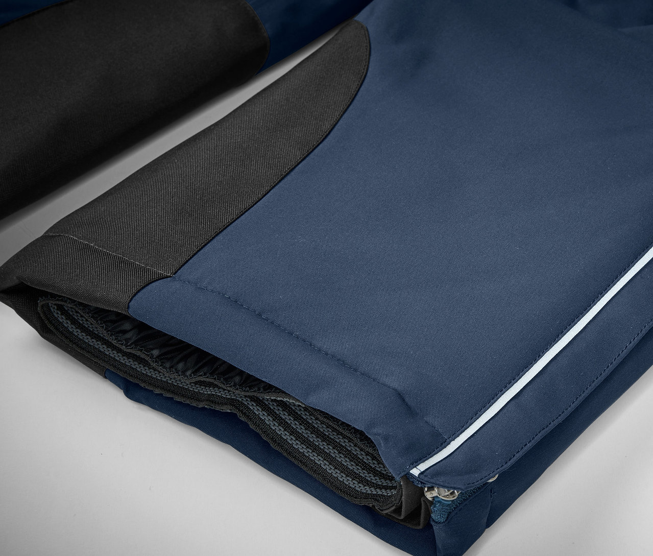 Detail einer blauen Hose mit schwarzen Details und einem weißen Streifen.