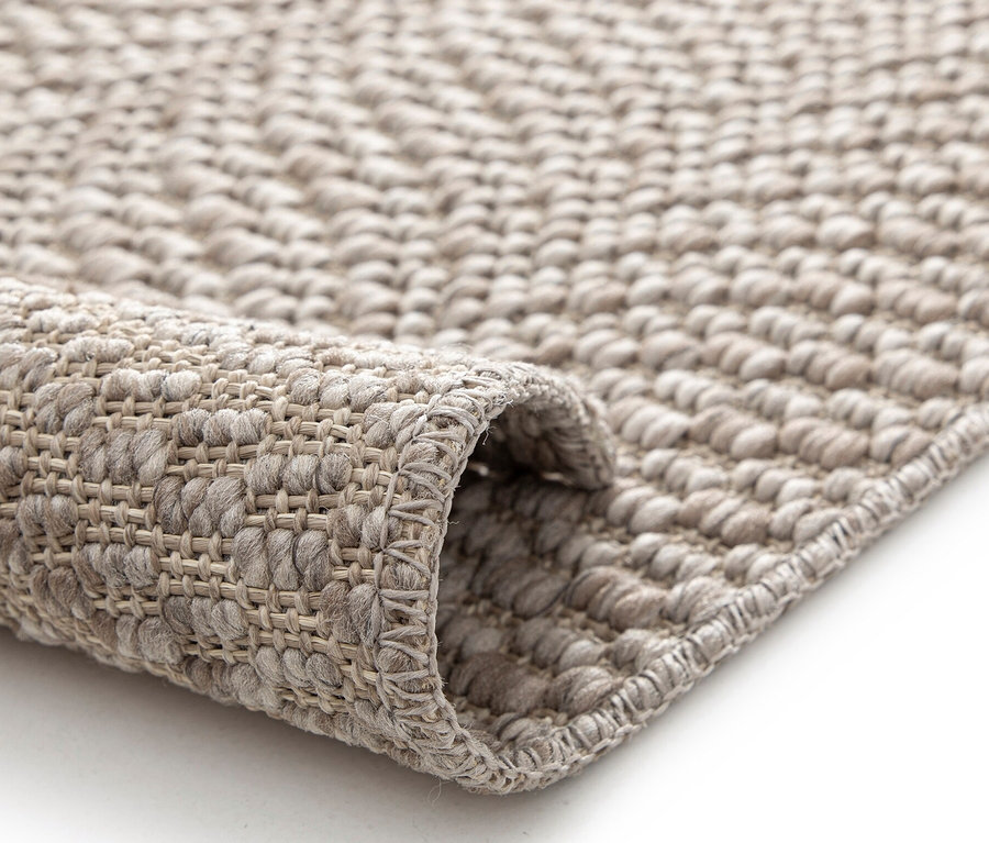 Nahaufnahme eines beigen Teppichs »Twine« auf einem weißen Untergrund, teilweise aufgerollt.
