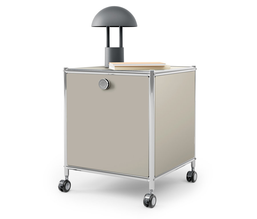 Auf der Oberseite eines beigen Rollcontainers stehen eine graue Lampe und ein Buch.